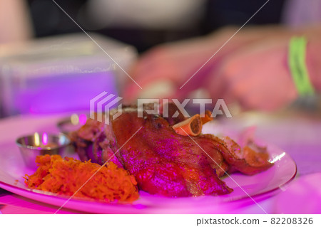 Unusual plate with pork knuckle. Unusual wooden plate with delicious pork knuckle and side dishes upon. 82208326