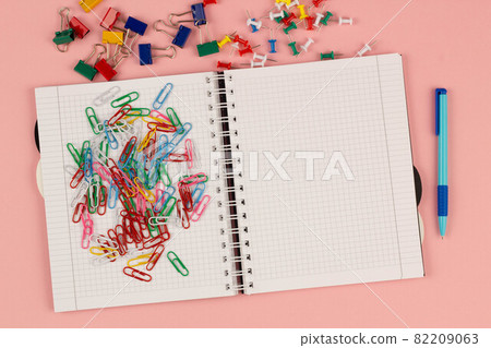 Open school squared notebook and colorful clips on the pink background. Blank white sheet of paper book on the table. Office supplies on the desktop. Back to school. Copy space for text. Top view Open school squared notebook and colorful clips on the pink background. Blank white sheet of paper book on the table. Office supplies on the desktop. Back to school. Copy space for text. Top view 82209063