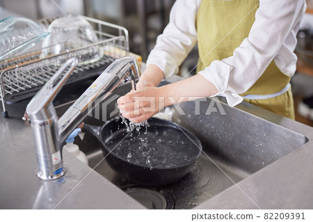 A young woman in an apron cleaning up in the kitchen 82209391