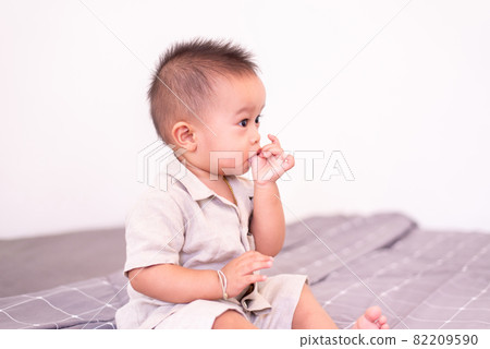 Adorable asian baby boy sucking thumb while sitting in bedroom,Happy new born kid 82209590