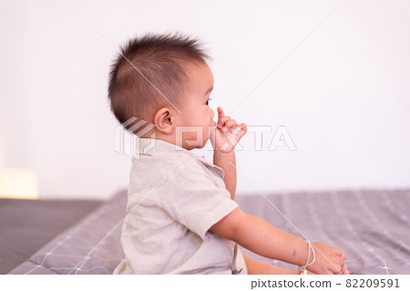 Adorable asian baby boy sucking thumb while sitting in bedroom,Happy new born kid 82209591