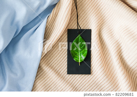 Green leaf on clothing tag and organic fabric background, sustainable fashion and brand label concept Green leaf on clothing tag and organic fabric background, sustainable fashion and brand label concept 82209681