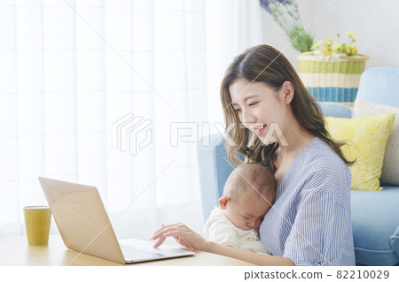 A mother holding a baby and using a computer A mother holding a baby and using a computer 82210029