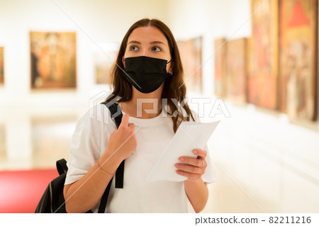 Young girl in a protective mask visits an exhibition of paintings in a museum 82211216