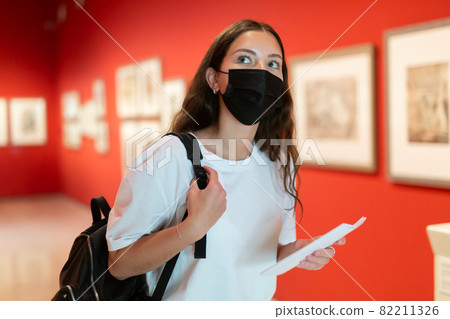 Young girl in a protective mask visits an exhibition of paintings in a museum 82211326