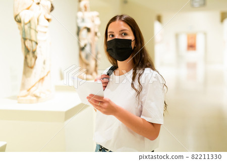 Young girl wearing a protective mask in the museum looks at the exhibits 82211330