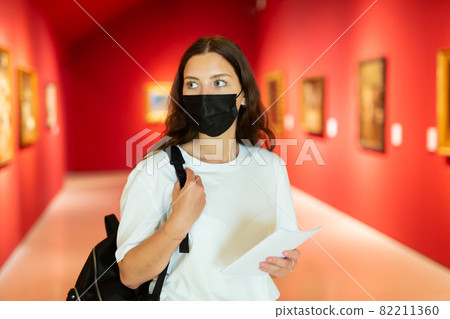 Young girl in a protective mask visits an exhibition of paintings in a museum 82211360