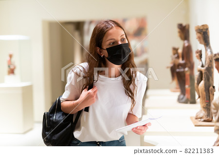 Young girl wearing a protective mask in the museum looks at the exhibits Young girl wearing a protective mask in the museum looks at the exhibits 82211383
