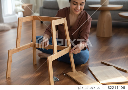 Focused indian woman use simple tools collect self assembly furniture 82211406