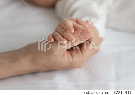 New mom holding little hand of sleeping newborn baby New mom holding little hand of sleeping newborn baby 82211411