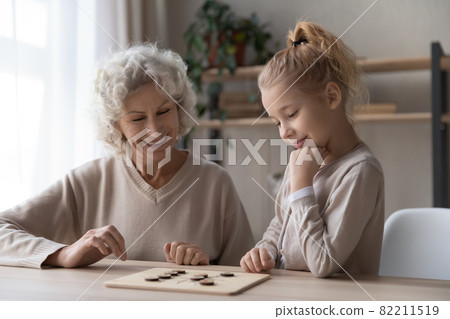 Old grandmother playing draughts with adorable little child girl. Old grandmother playing draughts with adorable little child girl. 82211519