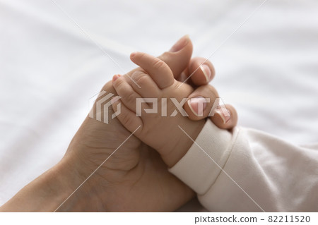 Young mom touching little palm of little baby Young mom touching little palm of little baby 82211520