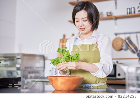 A young woman in an apron serving lettuce in the kitchen A young woman in an apron serving lettuce in the kitchen 82214253