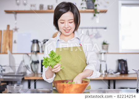 A young woman in an apron serving lettuce in the kitchen 82214254