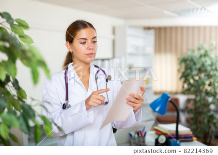 Young female doctor reading patient medical card in office Young female doctor reading patient medical card in office 82214369