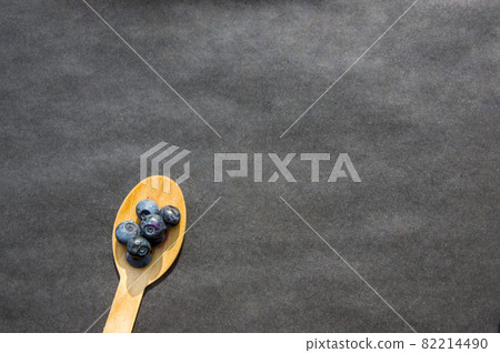 Flat lay of recycled spoon and juicy fresh blueberries on rough table. Space for text. Isolated ripe sweet bilberry fruits in eco spoon on black background. Copyspace. Healthy raw vegetarian food Flat lay of recycled spoon and juicy fresh blueberries on rough table. Space for text. Isolated ripe sweet bilberry fruits in eco spoon on black background. Copyspace. Healthy raw vegetarian food 82214490