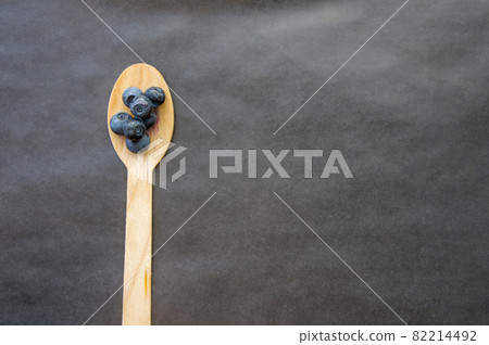 Flat lay of recycled spoon and juicy fresh blueberries on rough table. Space for text. Isolated ripe sweet bilberry fruits in eco spoon on black background. Copyspace. Healthy raw vegetarian food  82214492