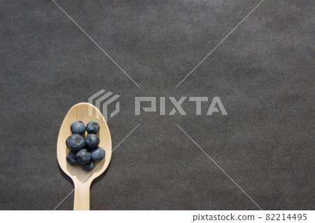 Flat lay of recycled spoon and juicy fresh blueberries on rough table. Space for text. Isolated ripe sweet bilberry fruits in eco spoon on black background. Copyspace. Healthy raw vegetarian food Flat lay of recycled spoon and juicy fresh blueberries on rough table. Space for text. Isolated ripe sweet bilberry fruits in eco spoon on black background. Copyspace. Healthy raw vegetarian food 82214495