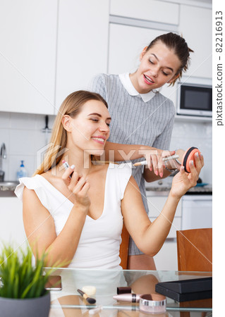Girl doing make-up for female friend at table with cosmetics in home Girl doing make-up for female friend at table with cosmetics in home 82216913