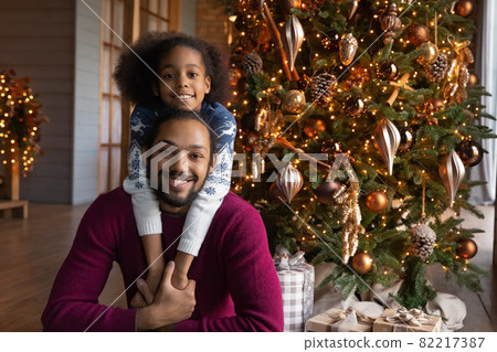 Portrait of biracial dad and daughter near fir tree 82217387