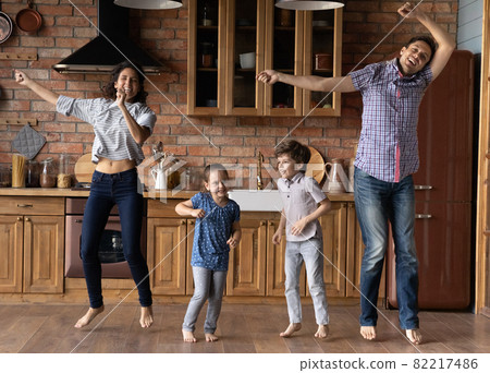 Happy young parents jumping with cute children in kitchen. Happy young parents jumping with cute children in kitchen. 82217486