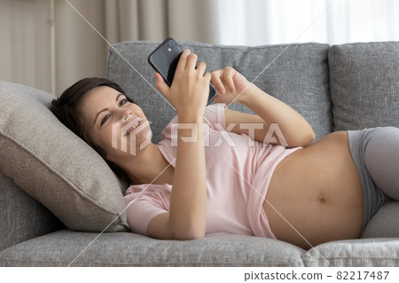Happy expectant female relax on soft couch using phone Happy expectant female relax on soft couch using phone 82217487