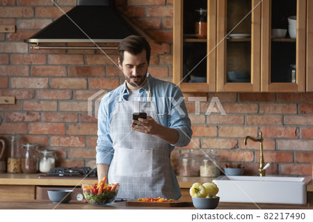 Bearded man using smartphone, distracted from cooking in kitchen Bearded man using smartphone, distracted from cooking in kitchen 82217490
