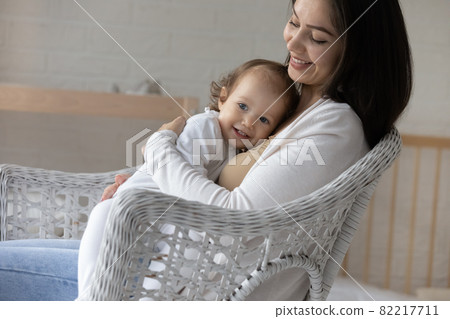 Smiling young mom hugging and cuddling little baby daughter Smiling young mom hugging and cuddling little baby daughter 82217711