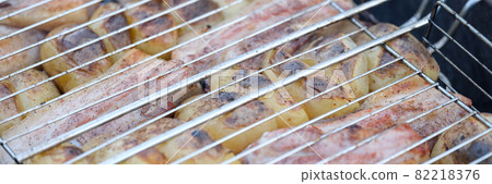 Roast pork and potatoes on wire rack over fire closeup 82218376