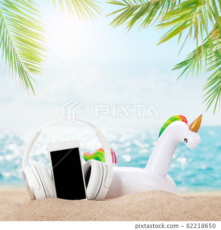 Smartphone, headphones and inflatable unicorn on tropical sea beach Smartphone, headphones and inflatable unicorn on tropical sea beach 82218650