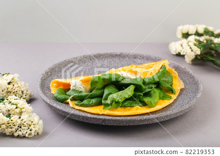 Omelette stuffed with spinach and cheese for a breakfast, with flowers on table Omelette stuffed with spinach and cheese for a breakfast, with flowers on table 82219353