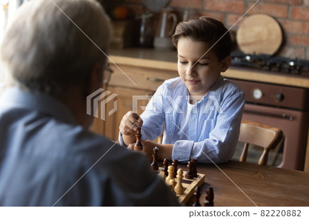 Little grandson with senior grandfather playing chess at home together 82220882