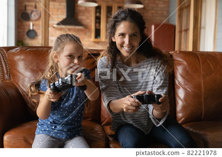 Happy small kid daughter playing video game with caring mother. Happy small kid daughter playing video game with caring mother. 82221978