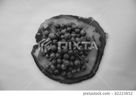 Flat lay of blue agate gemstone and juicy, fresh blueberries on black table. Isolated sweet bilberry fruits on translucent crystal surface on white background. Copy Space. Healthy raw vegetarian food  82223652