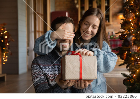 Happy young woman giving surprise Christmas gift to husband. Happy young woman giving surprise Christmas gift to husband. 82223860