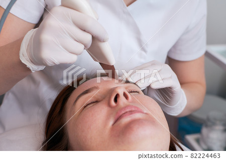 Ultrasonic facial cleansing is a modern and safe deep facial cleansing procedure. Woman at the reception at the beautician during spa procedures. 82224463