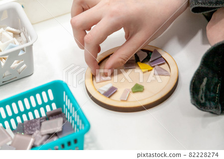 Master class on making mosaic panels. Close-up of the hands of a girl student taking a piece. 82228274