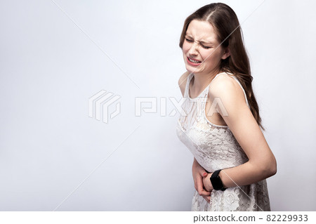 woman with freckles and white dress and smart watch with stomach pain on silver gray background. 82229933