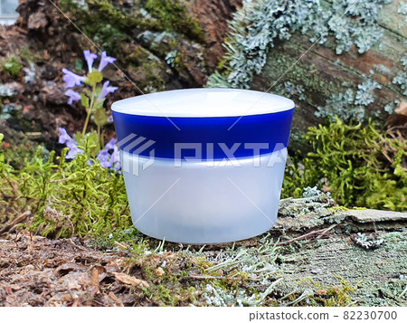 White cosmetic jar with blue screw cap and green forest moss. Front view, mockup, closeup. Cosmetic bottle container with moisturizer for branding. White cosmetic jar with blue screw cap and green forest moss. Front view, mockup, closeup. Cosmetic bottle container with moisturizer for branding. 82230700