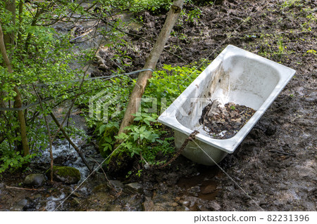 An old tub chained to a tree by a stream. Natural bathroom. 82231396
