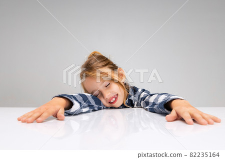 Portrait of beautiful little girl looking at camera, making faces isolated on gray studio background. Human emotions, facial expression concept. Portrait of beautiful little girl looking at camera, making faces isolated on gray studio background. Human emotions, facial expression concept. 82235164