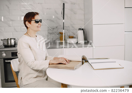 Blind mature woman reading braille book at home 82236479