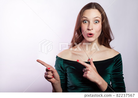 Portrait of surprised shocked woman with classic green dress showing empty space with finger. 82237567