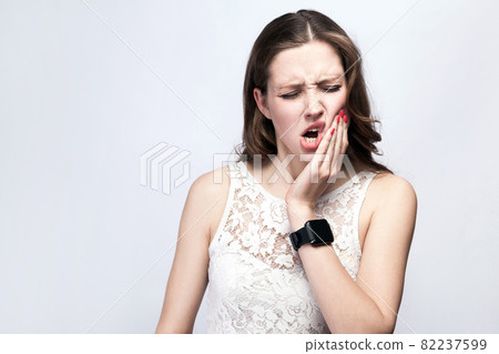 woman with freckles and white dress and smart watch with tooth pain on silver gray background. 82237599