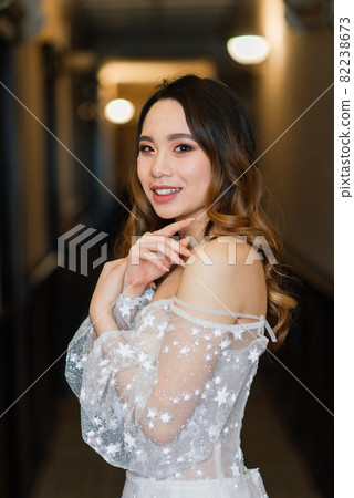 Gorgeous young asian woman in elegant dress looking at camera and window, morning of bride, wedding Gorgeous young asian woman in elegant dress looking at camera and window, morning of bride, wedding 82238673