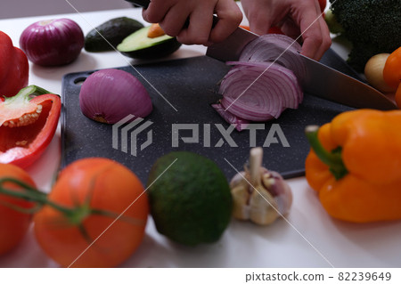 Chef cutting red onion on board among vegetables closeup Chef cutting red onion on board among vegetables closeup 82239649