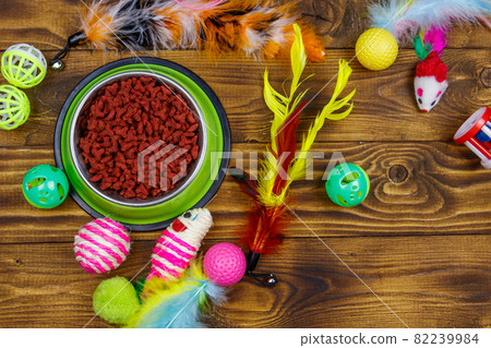 Set of toys for cat and bowl with dry pet food on wooden background. Top view. Pet care concept Set of toys for cat and bowl with dry pet food on wooden background. Top view. Pet care concept 82239984
