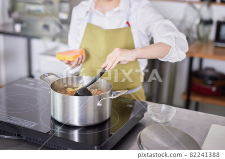 A young woman in an apron making curry in the kitchen 82241388