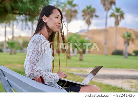 Young beautiful woman outdoors with laptop, tropical park background 82241420
