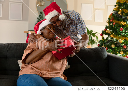 Happy african american couple wearing santa hats giving each other presents at christmas time 82245600
